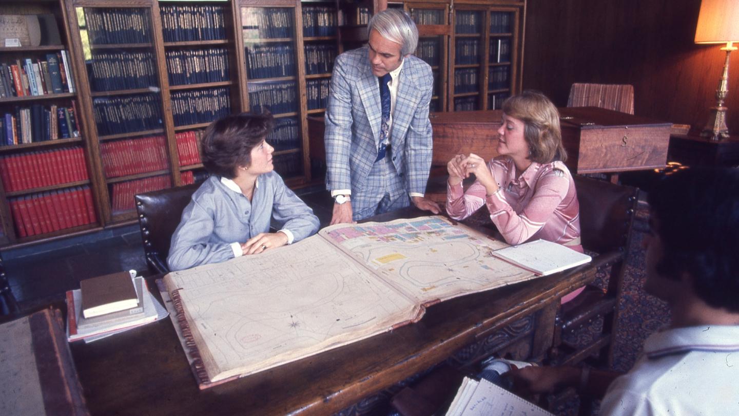 一个男人站着和两个女人聊天，同时看着澳门金沙线上赌博官网的校园地图.